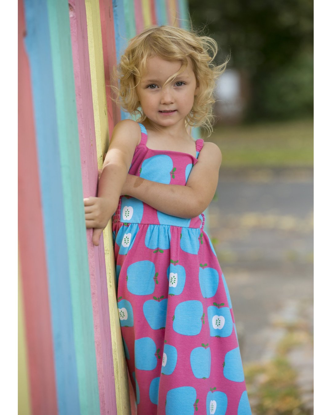 Kind mit süßem Sommerkleid mit Spagettiträgern und blauen Äpfeln auf Pink Hintergrund 