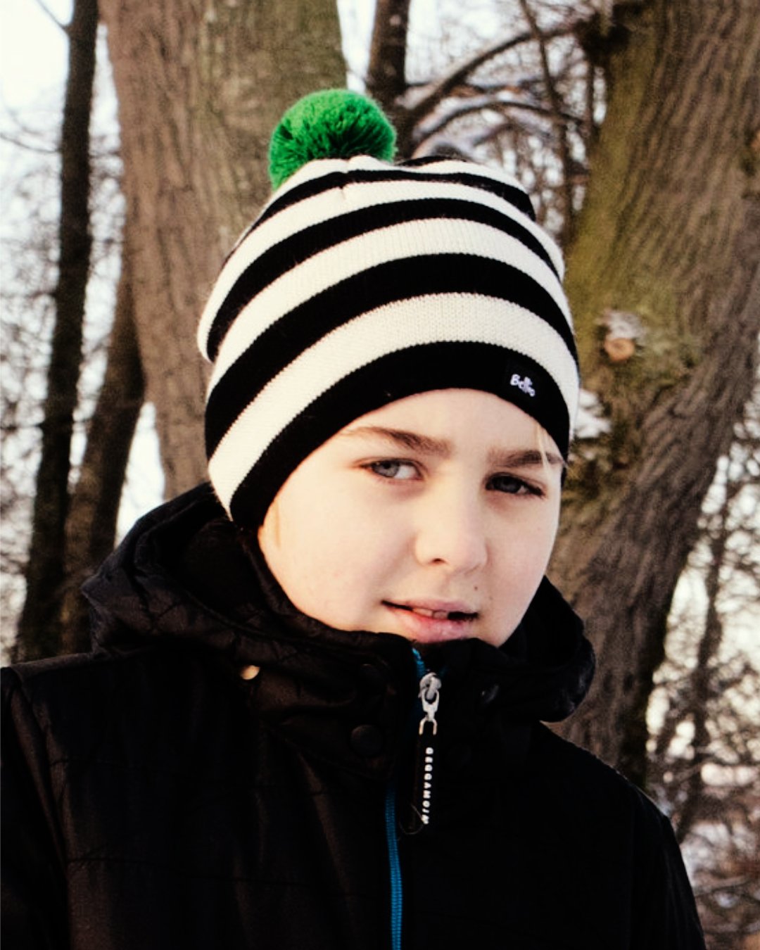 Junge mit gestreifter schwarz/weiß Strickmütze mit grüner Bommel aus Bio Wolle